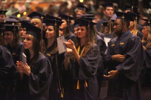 Students in purple robes applaud at graduation