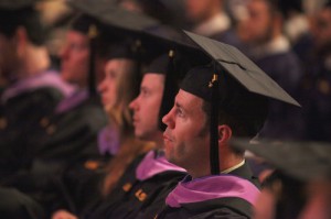 Line of people seated in black robes and caps at graduation ceremony