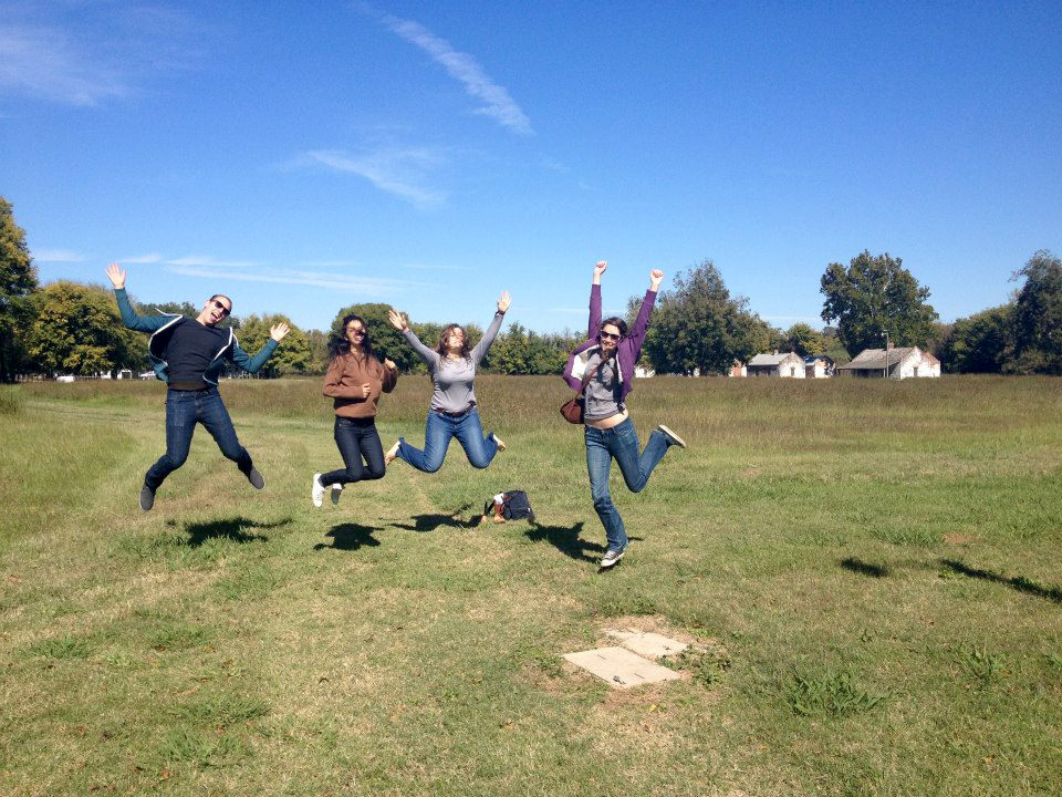 Female students jumping in grassy field, bright blue sky